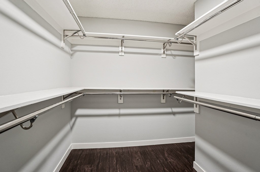A walk-in closet with white walls and wooden floors.
