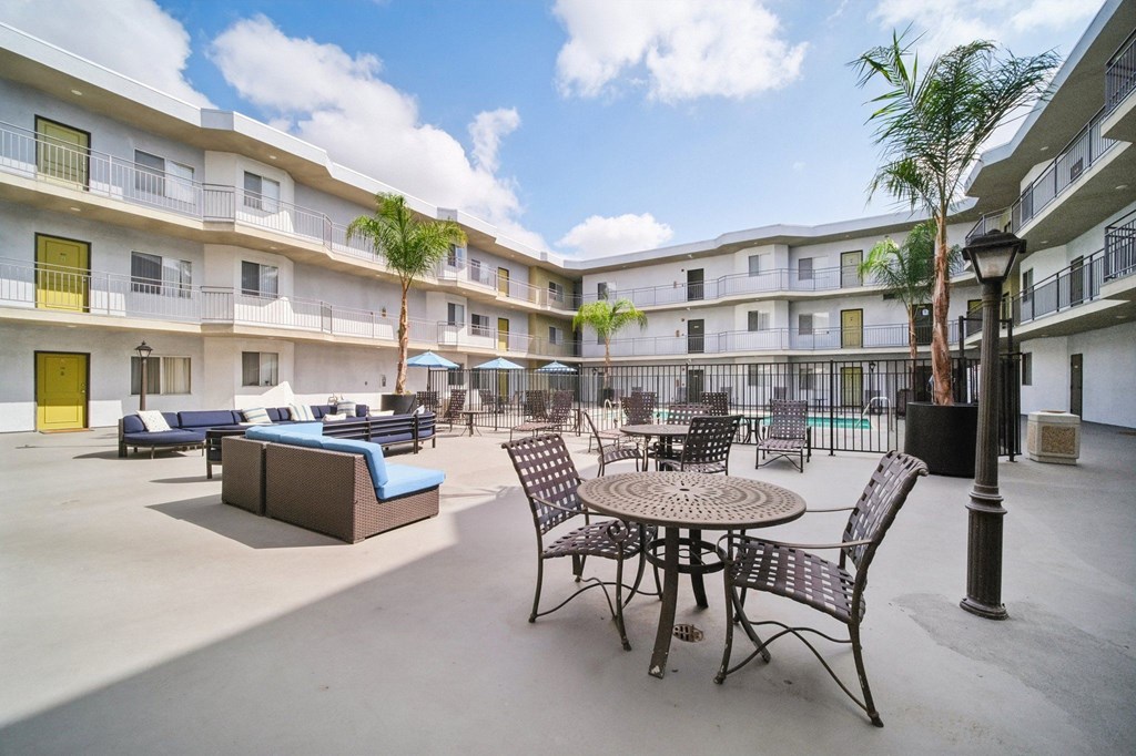 A patio area with tables and chairs and a pool in the background.