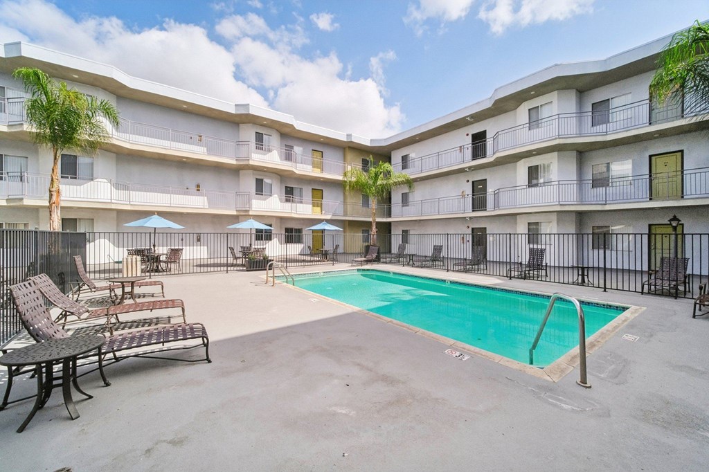 A pool area with chairs and a fence in front of a building.
