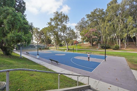A park with a blue basketball court and a metal railing.