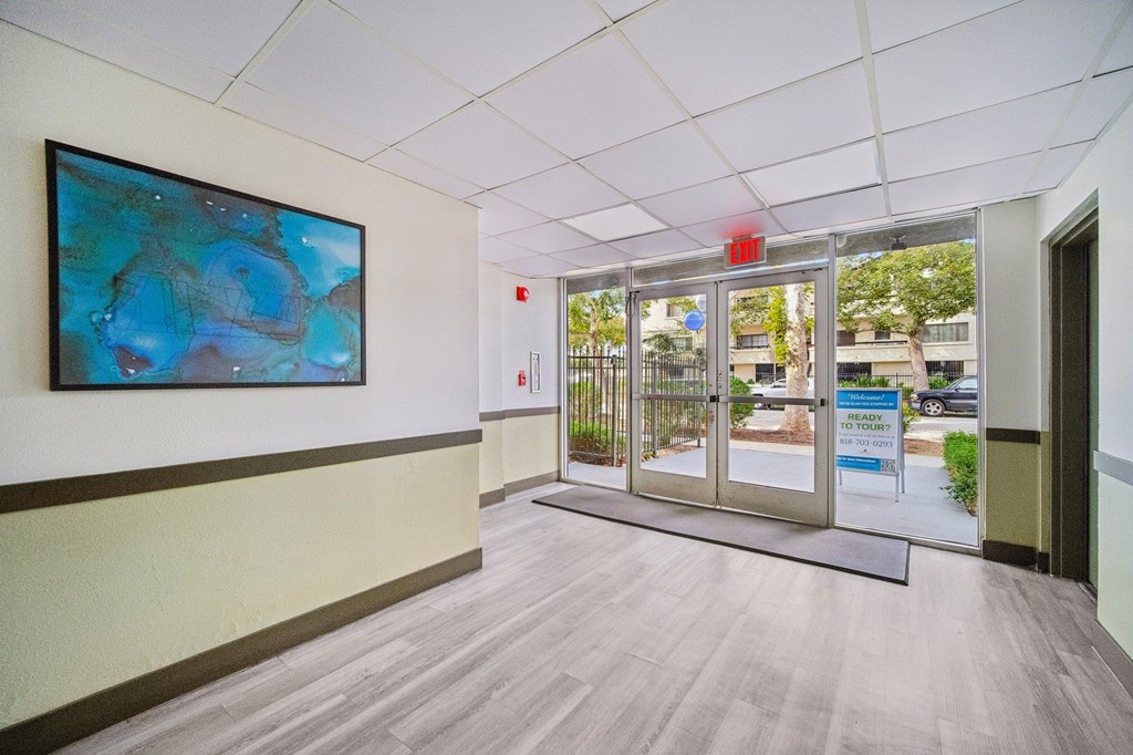 A hallway with a painting on the wall and a red exit sign above the door.