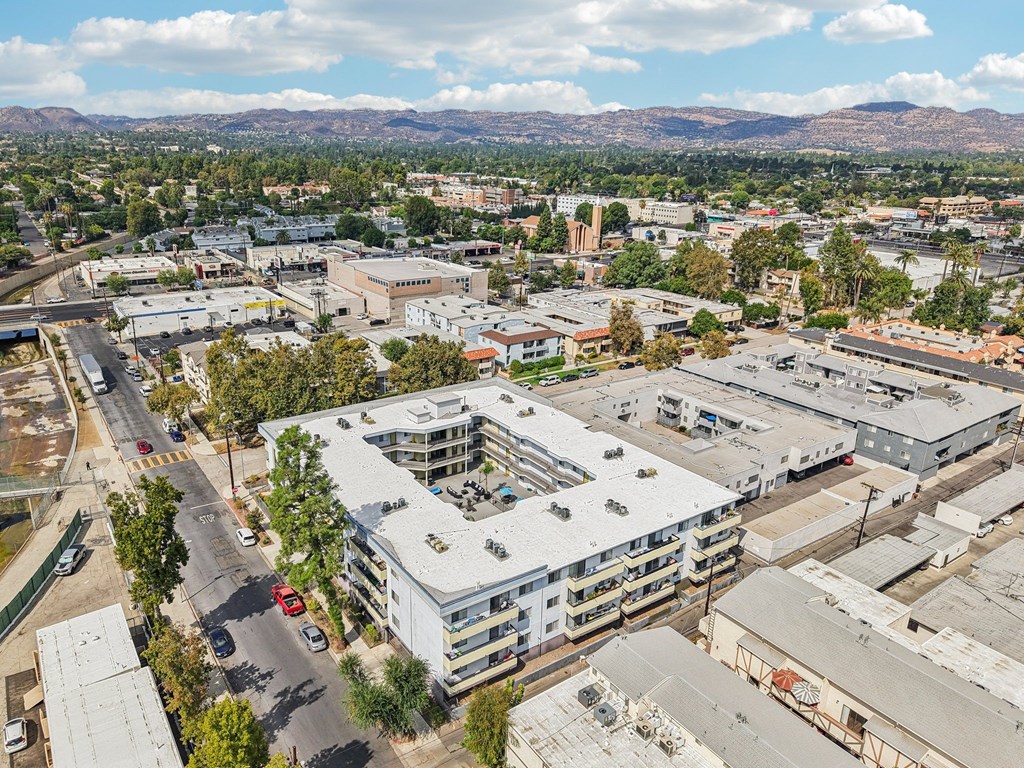 A large white building with a grey roof is surrounded by other buildings and trees.