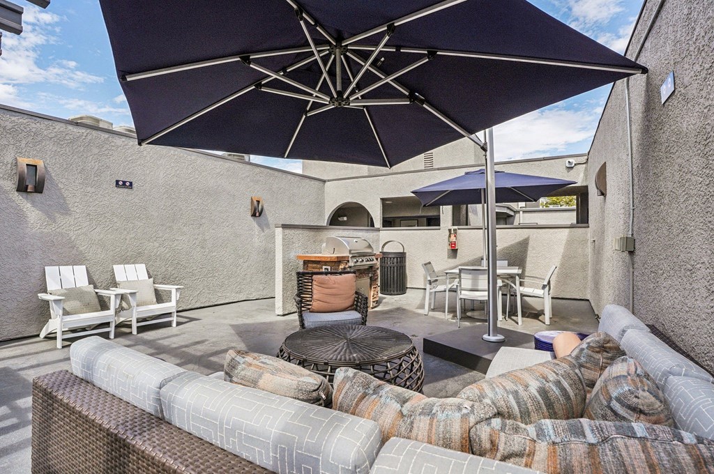 A patio with a couch, chairs, and an umbrella.
