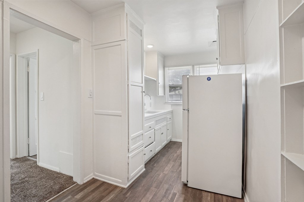 A white kitchen with a refrigerator, sink, and cabinets.