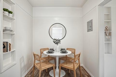 A small dining room with a round mirror and a table with chairs.