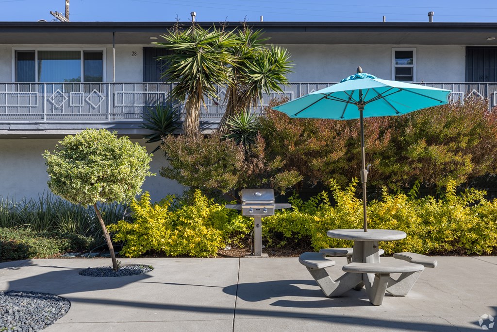 A blue umbrella is on a table in the middle of a courtyard.
