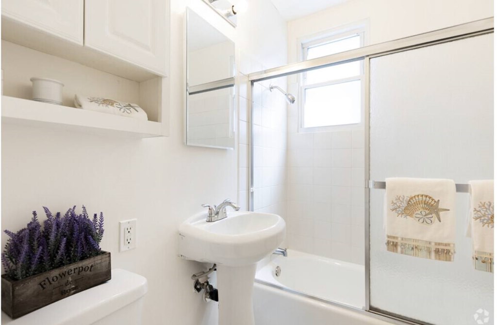 A white bathroom with a white sink and a white towel hanging on the shower door.