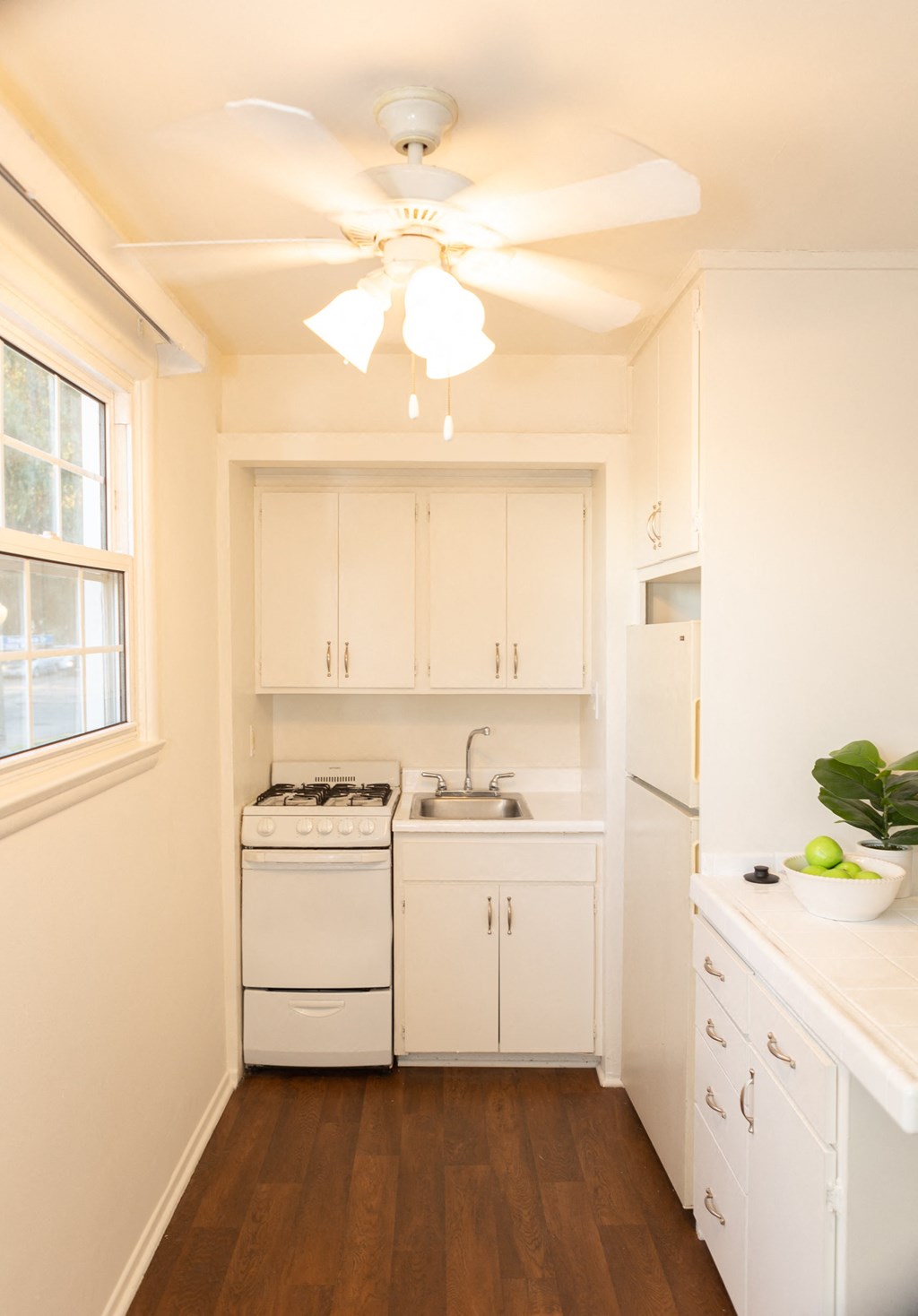 a small kitchen with white cabinets and a ceiling fan