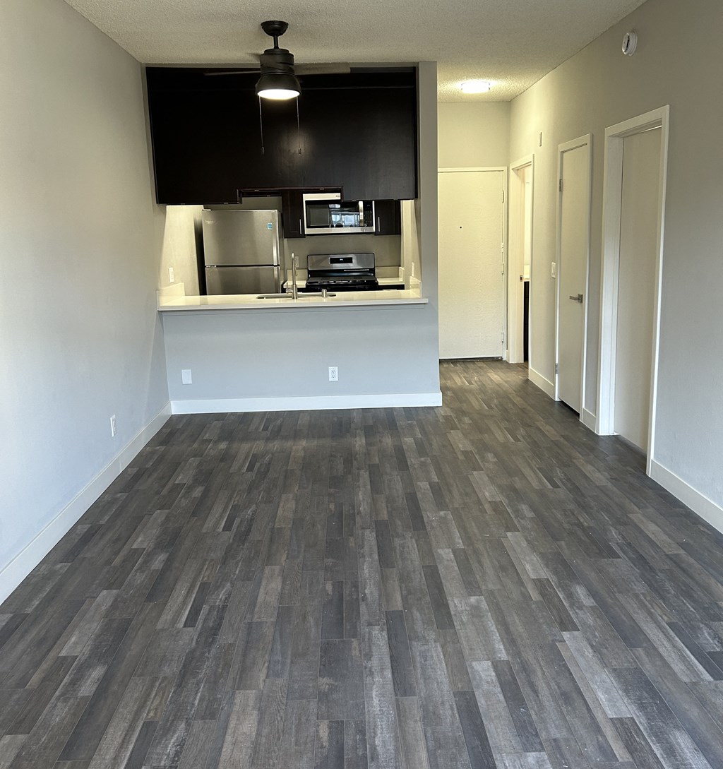 an empty living room with wood floors and a kitchen