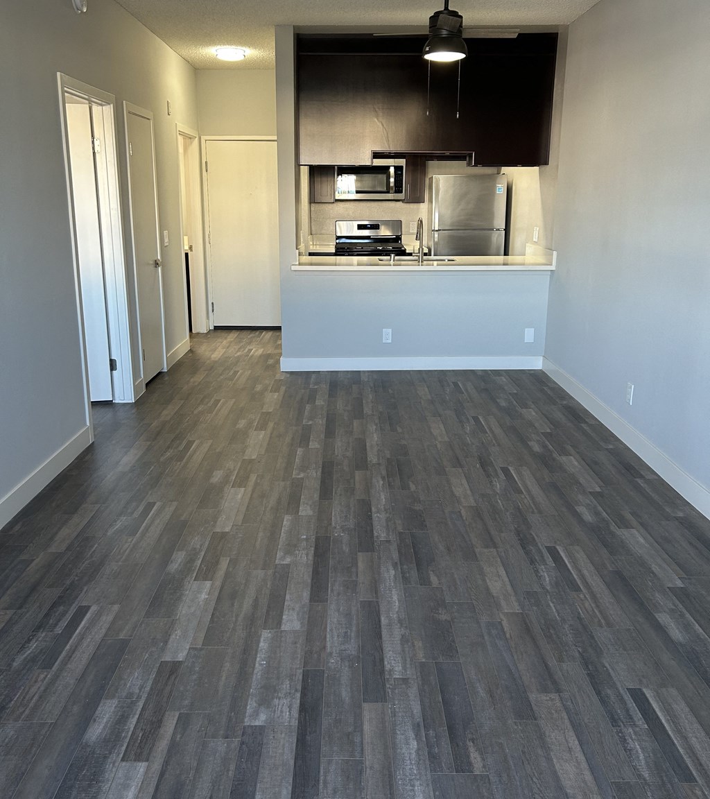 an empty living room with wood floors and a kitchen