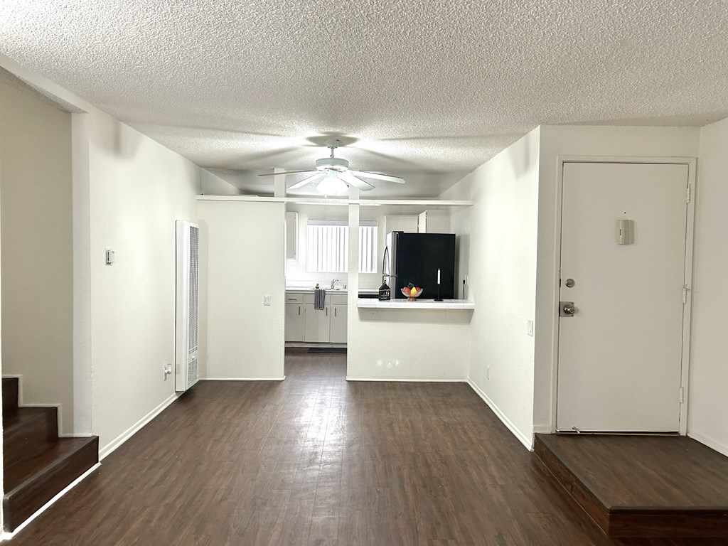 an empty living room with a ceiling fan and a kitchen