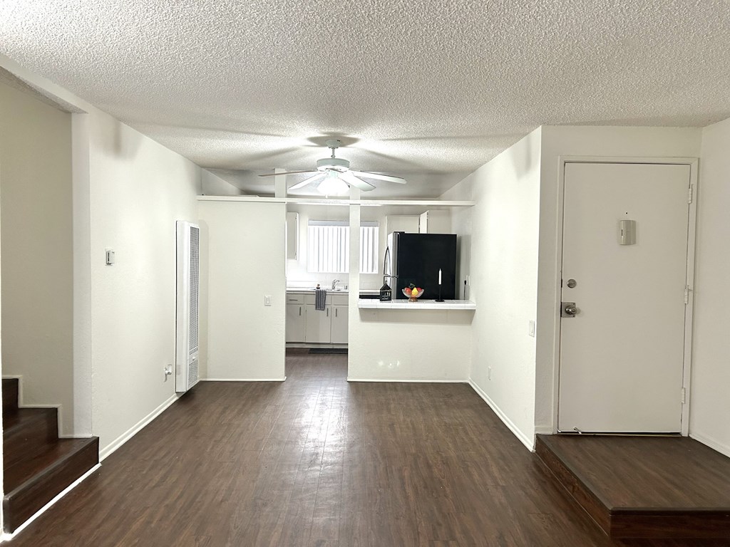 an empty living room with a ceiling fan and a kitchen