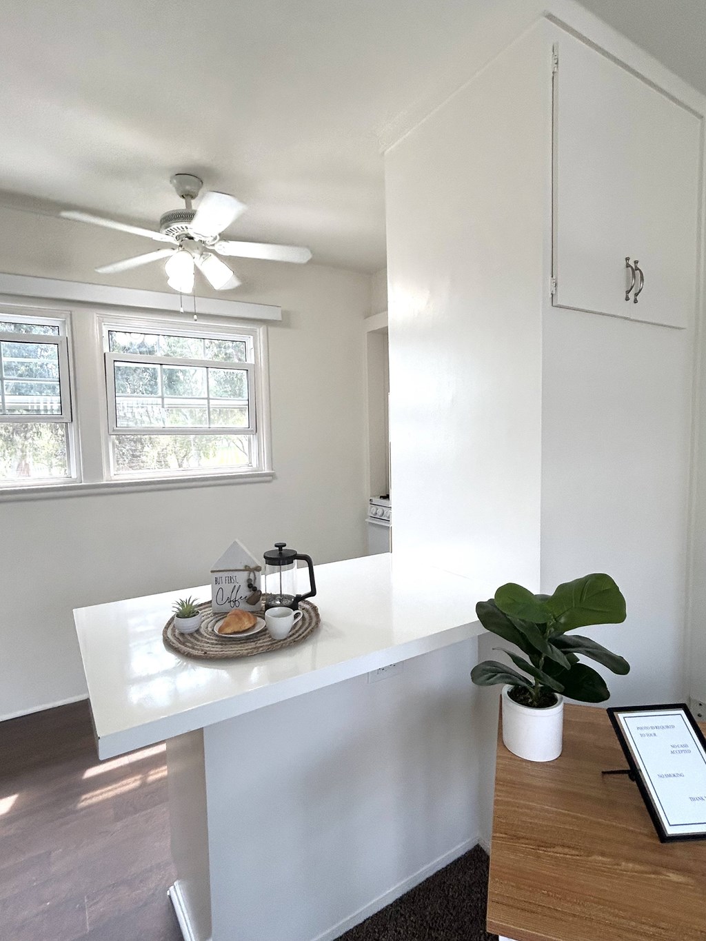 A white reception desk with a fan on the ceiling and a plant on the desk.