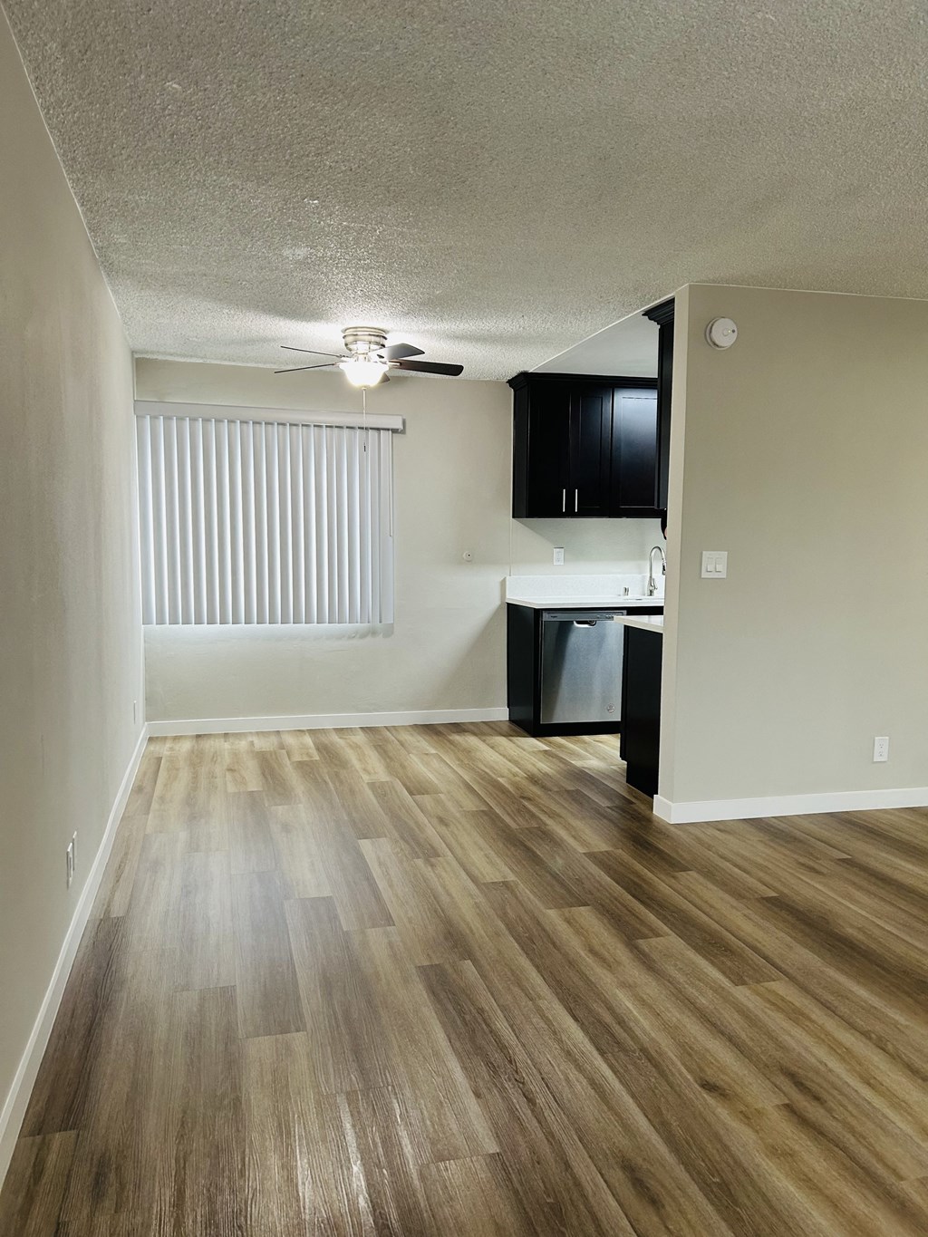 an empty living room and kitchen with wood flooring and a ceiling fan