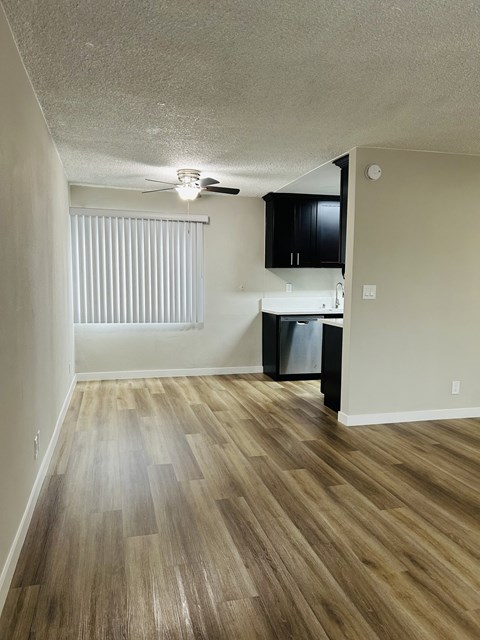 an empty living room and kitchen with wood flooring and a ceiling fan