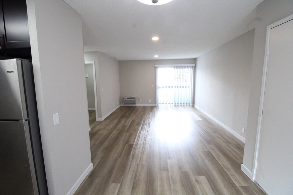 an empty living room with wood flooring and a refrigerator