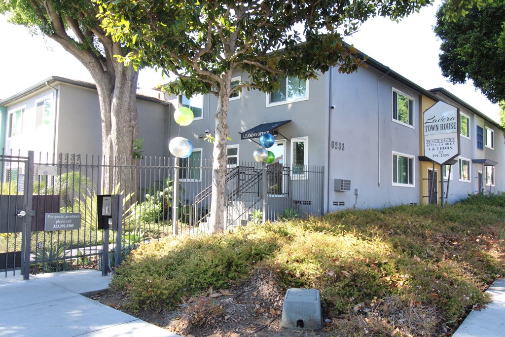 a gray building with a black fence and a tree in front of it