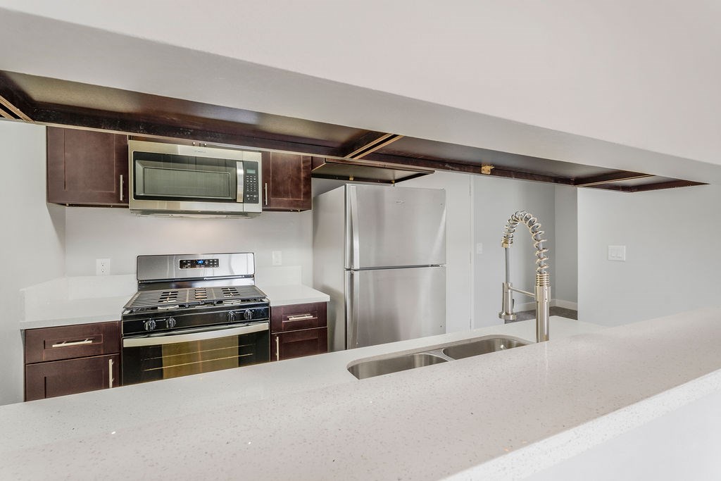 A kitchen with a stove, microwave, refrigerator, and sink.