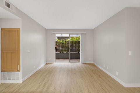 A room with a wooden door and a window with a view of a fence and trees.