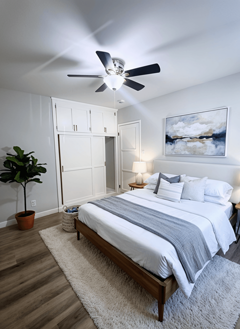 A bedroom with a bed, a ceiling fan, and a painting on the wall.