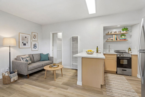 A modern kitchen and living room with a grey couch and wooden coffee table.