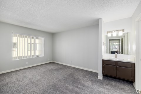 A spacious room with a window, carpeted floor, and a bathroom with a sink and mirror.