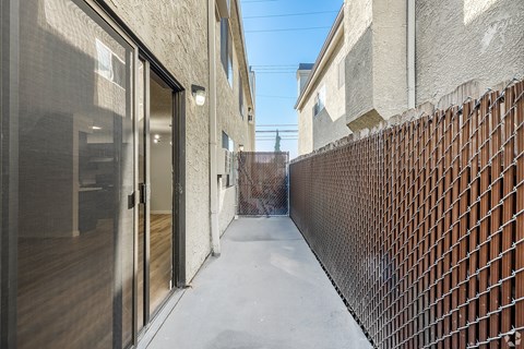 A narrow alley with a fence on one side and a building with a glass door on the other.