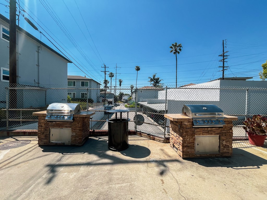 two bbq pits in a yard with a fence and buildings