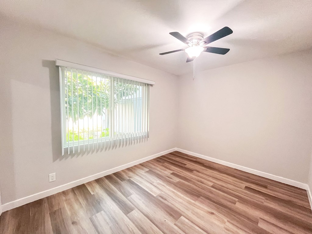 the spacious living room with hardwood flooring and a ceiling fan