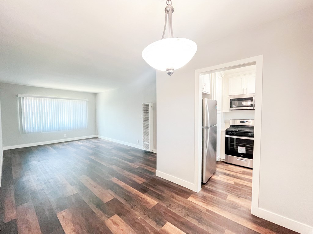 an empty living room and kitchen with wood flooring and a refrigerator