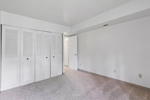 A room with white walls and a grey carpet with a row of white cupboards.