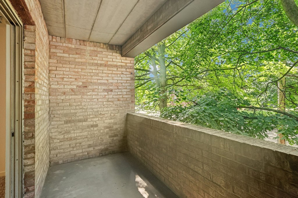 A balcony with a brick wall and a view of trees.
