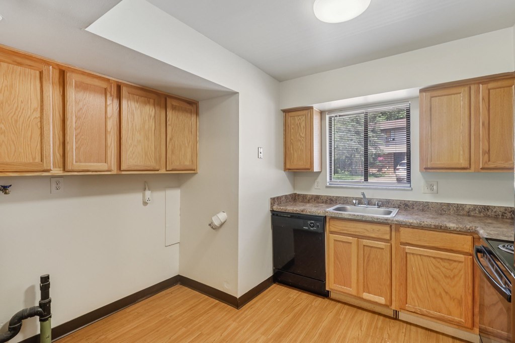 A kitchen with wooden cabinets and a black dishwasher.