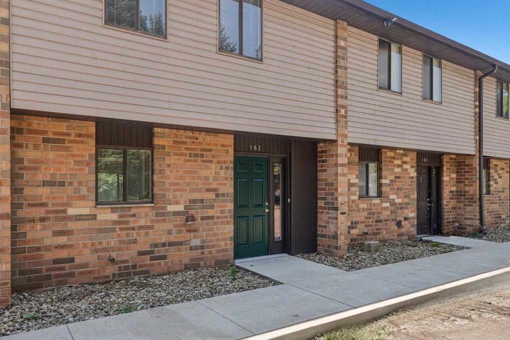 A row of houses with brown brick walls and green doors.