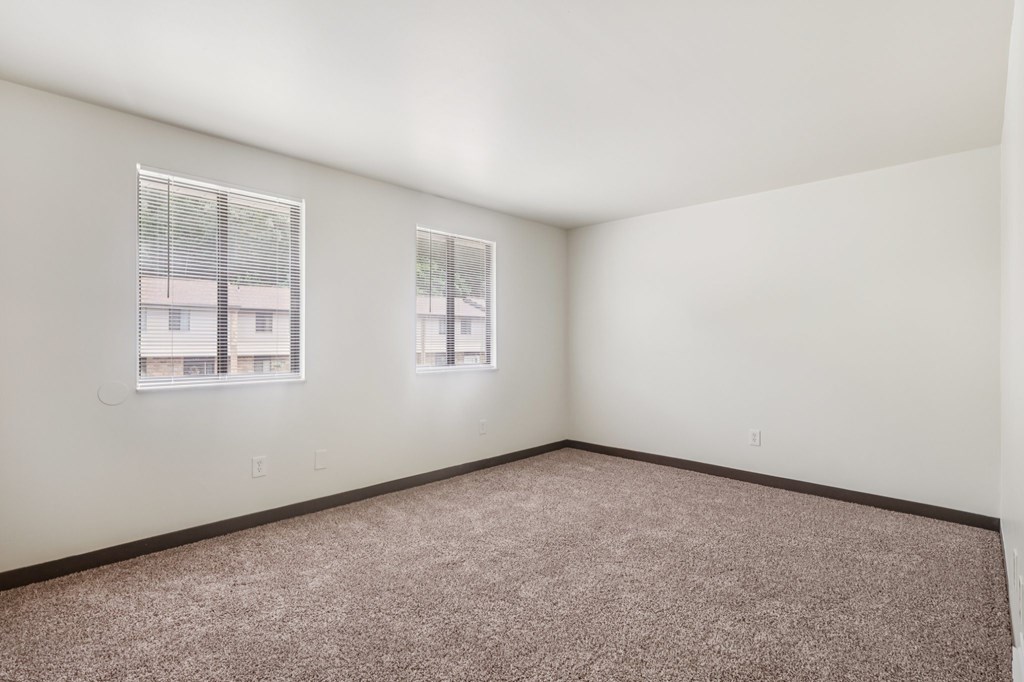 A room with carpeted floor and two windows.