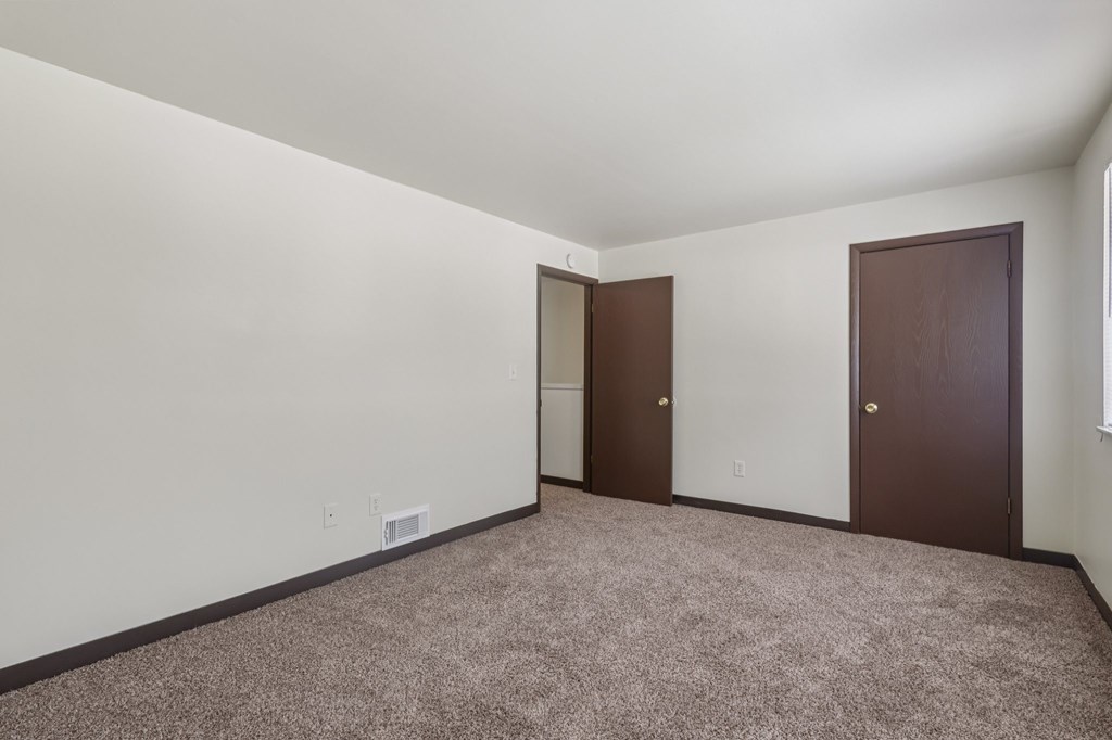 A room with two brown doors and carpeted floor.
