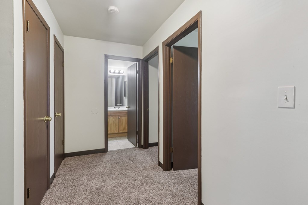 A hallway with a carpeted floor and a light switch on the wall.