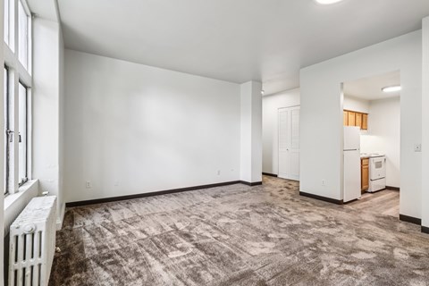 A spacious, empty room with a carpeted floor and a radiator on the left side.