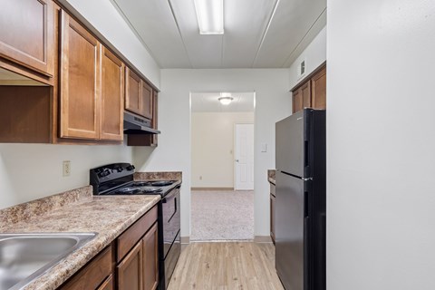 A kitchen with a black refrigerator and brown cabinets.