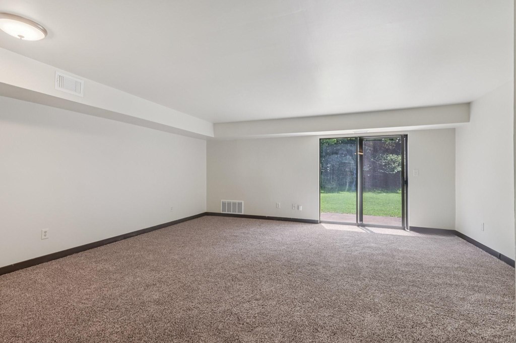 A room with a carpeted floor and a window with a view of trees.