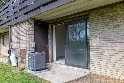 A grey air conditioning unit sits outside a brick building.