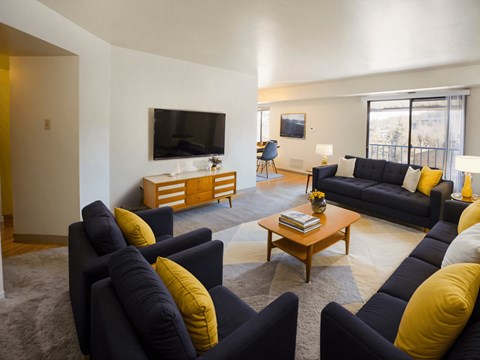 A living room with a black couch and yellow pillows.