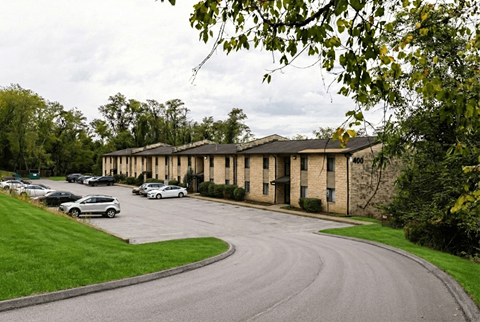 A curved driveway leads to a building with a parking lot in front.