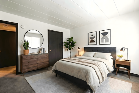A bedroom with a bed, nightstand, and a plant.