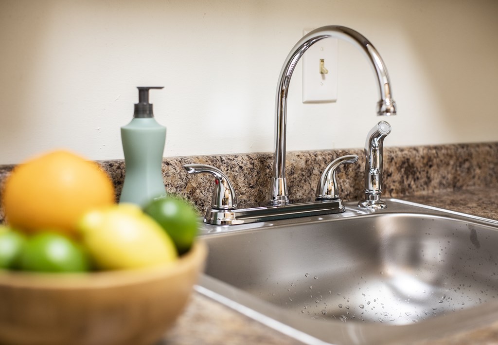 A bowl of fruit sits on a kitchen counter next to a sink.