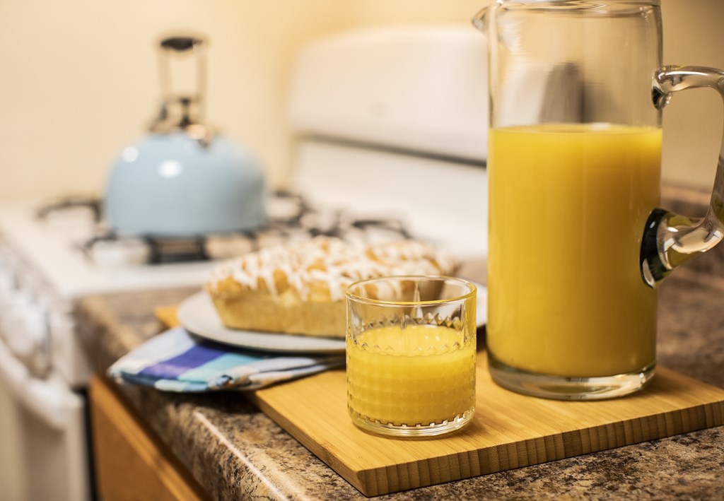A pitcher and a glass of orange juice on a wooden cutting board.