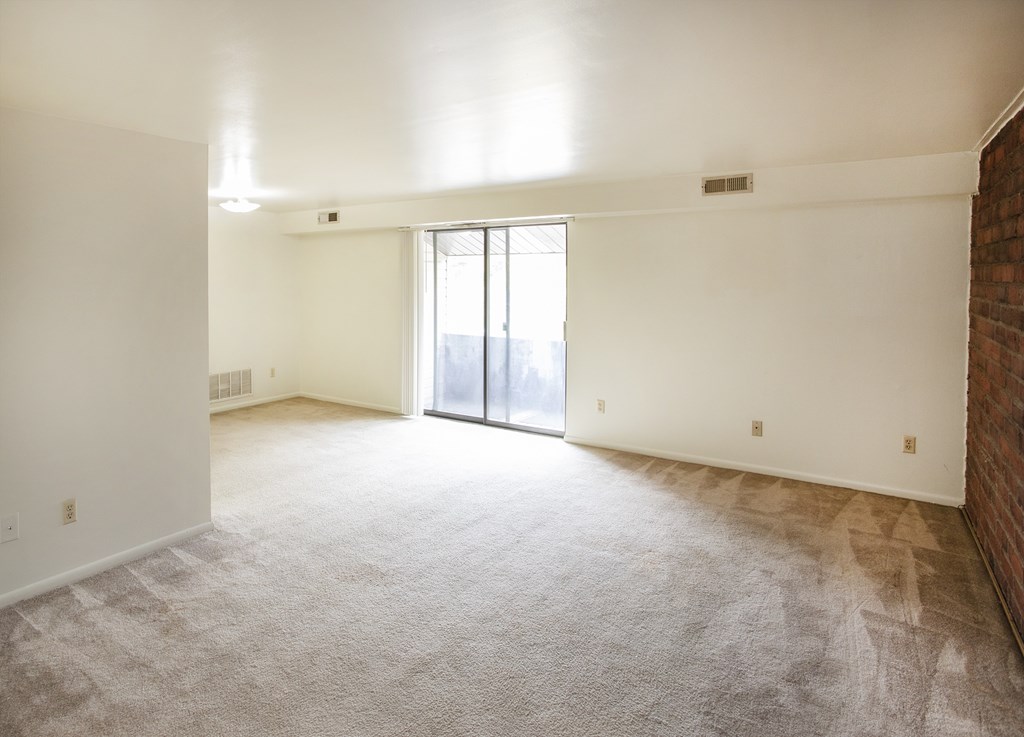A large, empty room with a carpeted floor and a sliding glass door leading to a balcony.