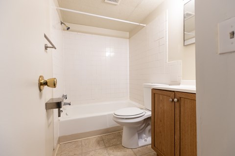 A white bathroom with a toilet, tub, and cabinet.