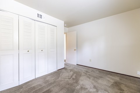 A room with white walls and a carpeted floor with three white doors.
