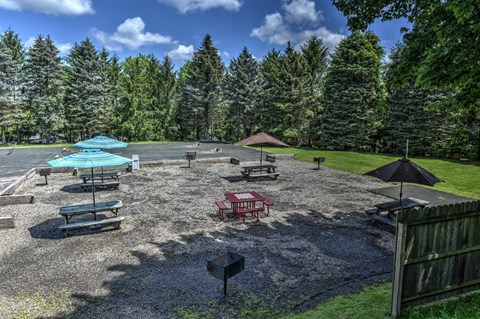 A gravel area with picnic tables and umbrellas surrounded by trees.